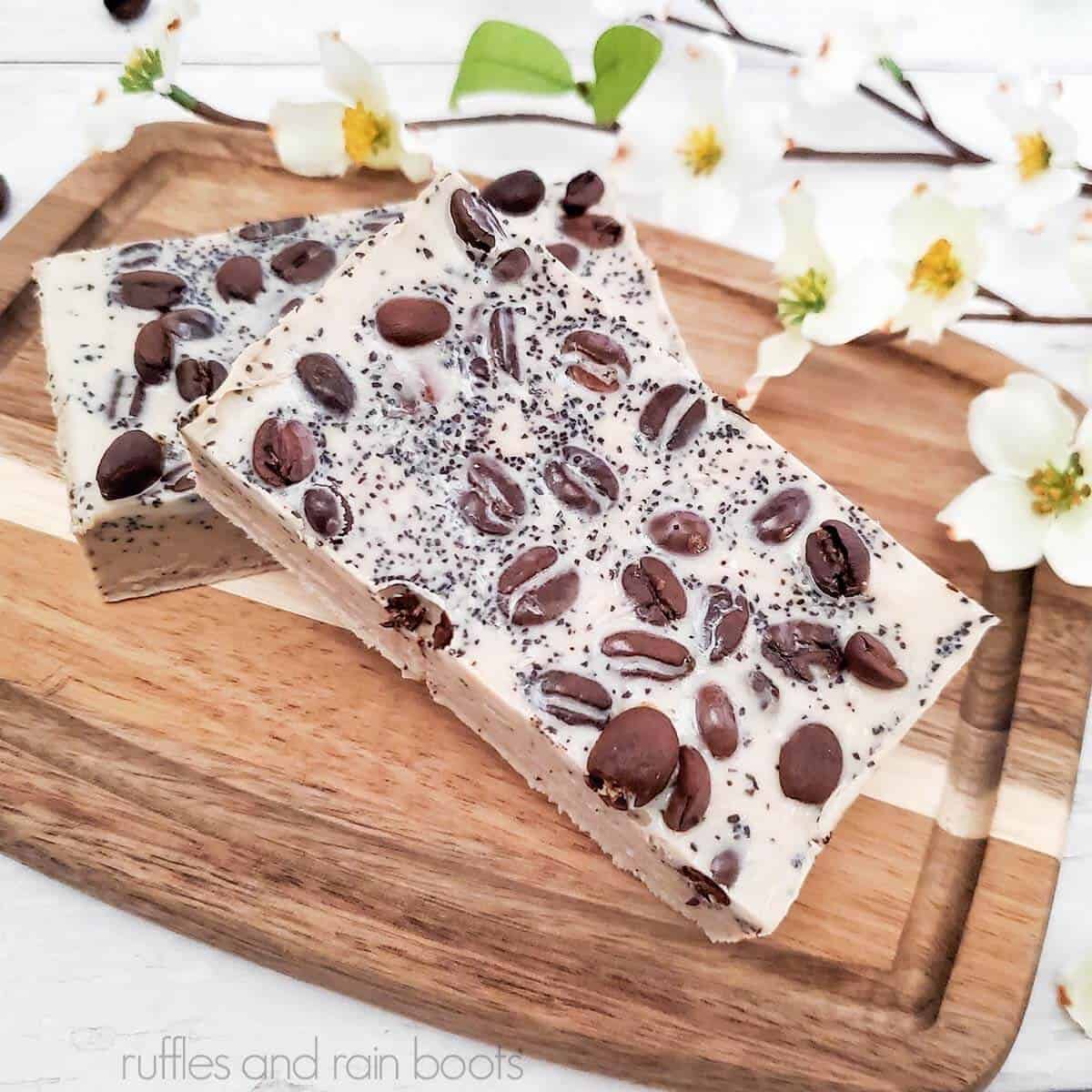 Square image close up of coffee soap on small wood cutting board with white flowers on white wood.