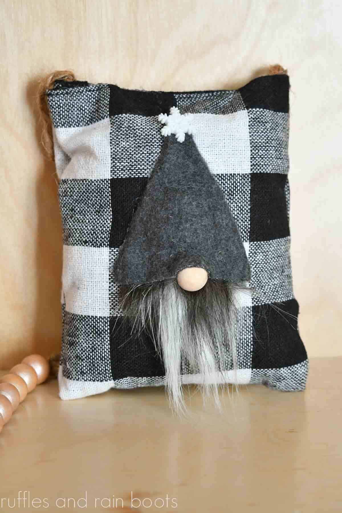 Vertical image of a gray hat gnome tiered tray pillow with a snowflake in front of a light colored wood background.