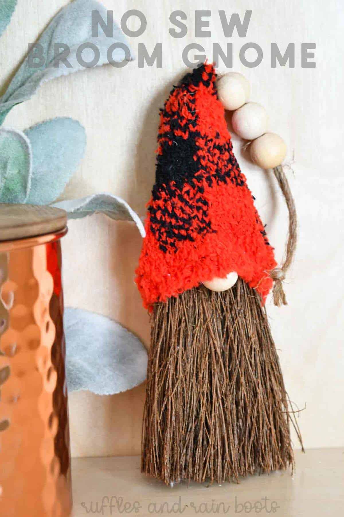 Vertical image of a gnome ornament with farmhouse hanger near a plant and copper pot with text which reads no sew broom gnome.