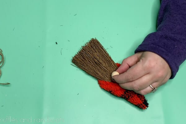 Crafter using hot glue to secure the wood bead onto the mini broom for a gnome nose.
