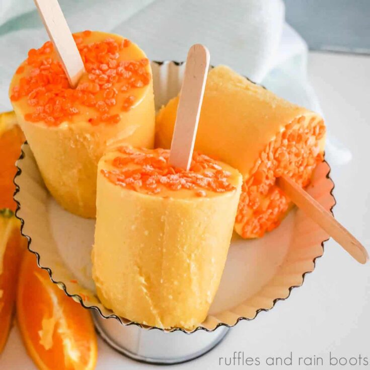 Square close up image of orange cream popsicles on a cake tray in front of a white dinner napkin on a white table.