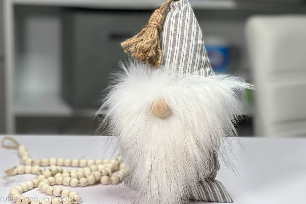 Horizontal close up image of a pillow gnome with a white beard, hickory fabric, and farmhouse tassel.