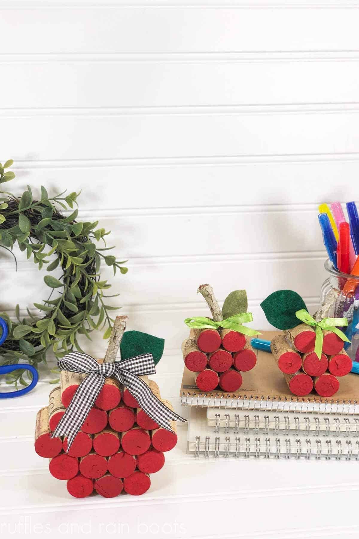 Vertical image of wine cork apples made for a back to school craft in front of a white background with school supplies and a wreath.
