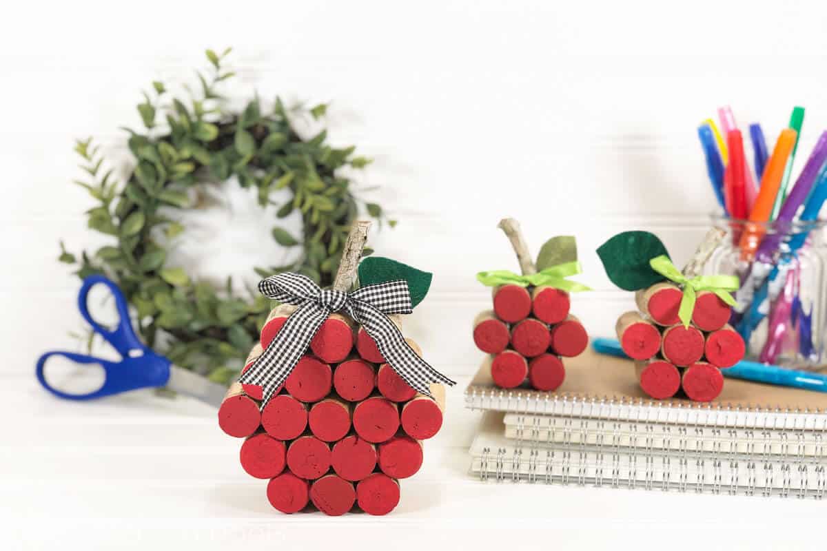 Horizontal image of three differently sized recycled wine cork apples with a wreath and school supplies.