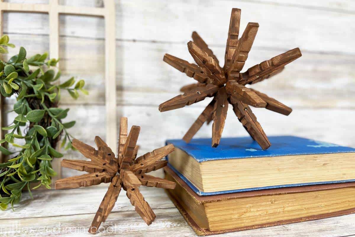 Horizontal image of two wood 3D stars made from clothespins next to vintage books on white wood background.