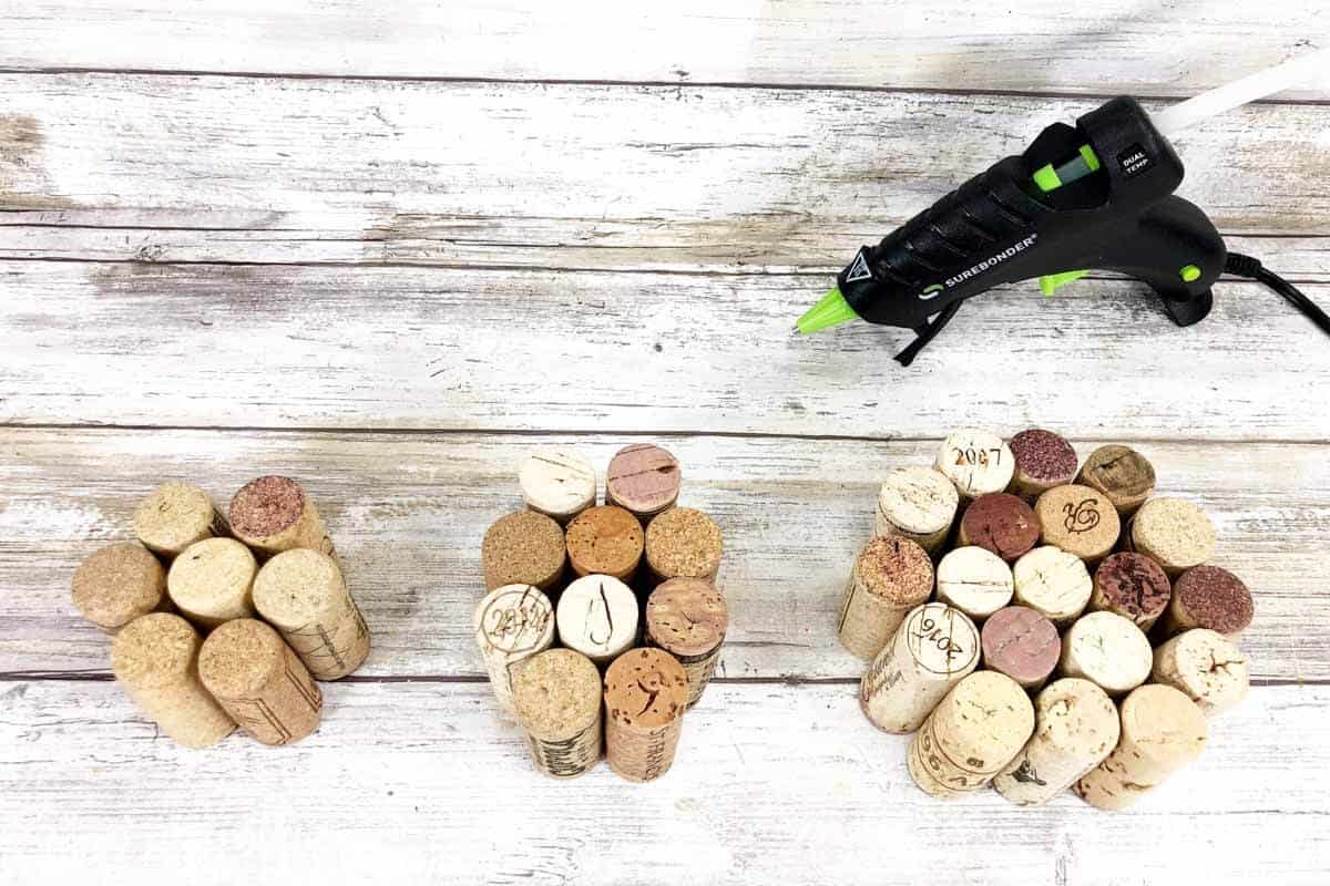 Three sets of wine cork apples on wood background with small glue gun.