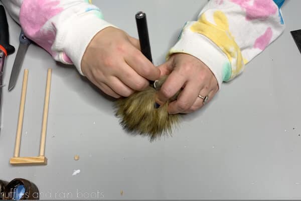 Crafter showing to use a craft knife to open a pre-made pompom to use as a gnome body.