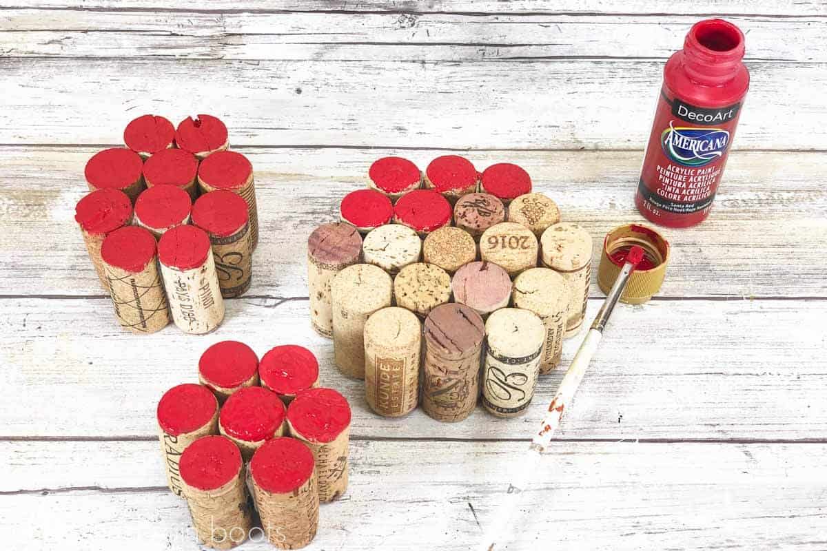 Paintbrush and red paint showing the fronts of all wine corks painted red to resemble an apple.