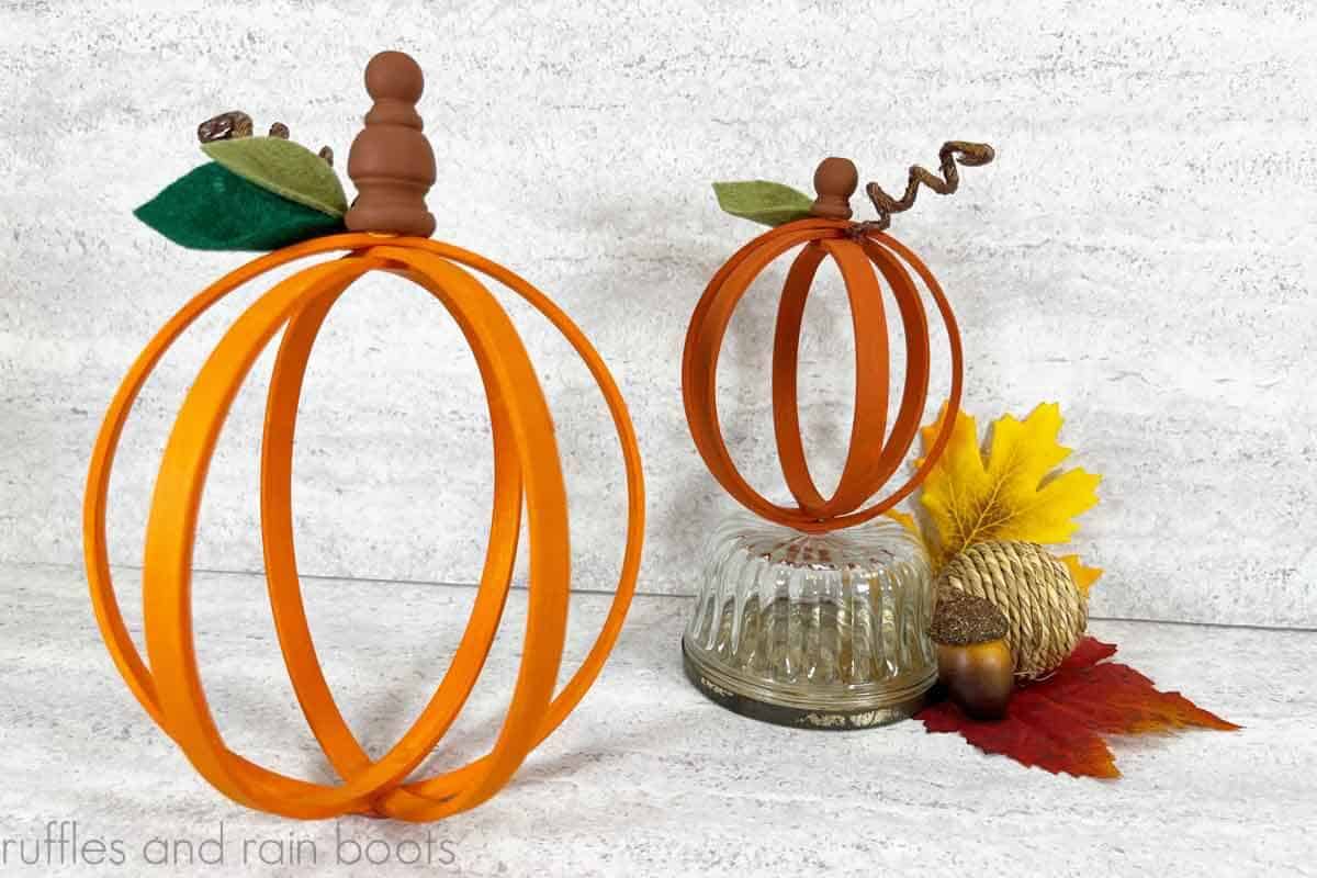 Horizontal close up image of orange pumpkins made with embroidery hoops, finials, felt, and twine displayed on a fall background.