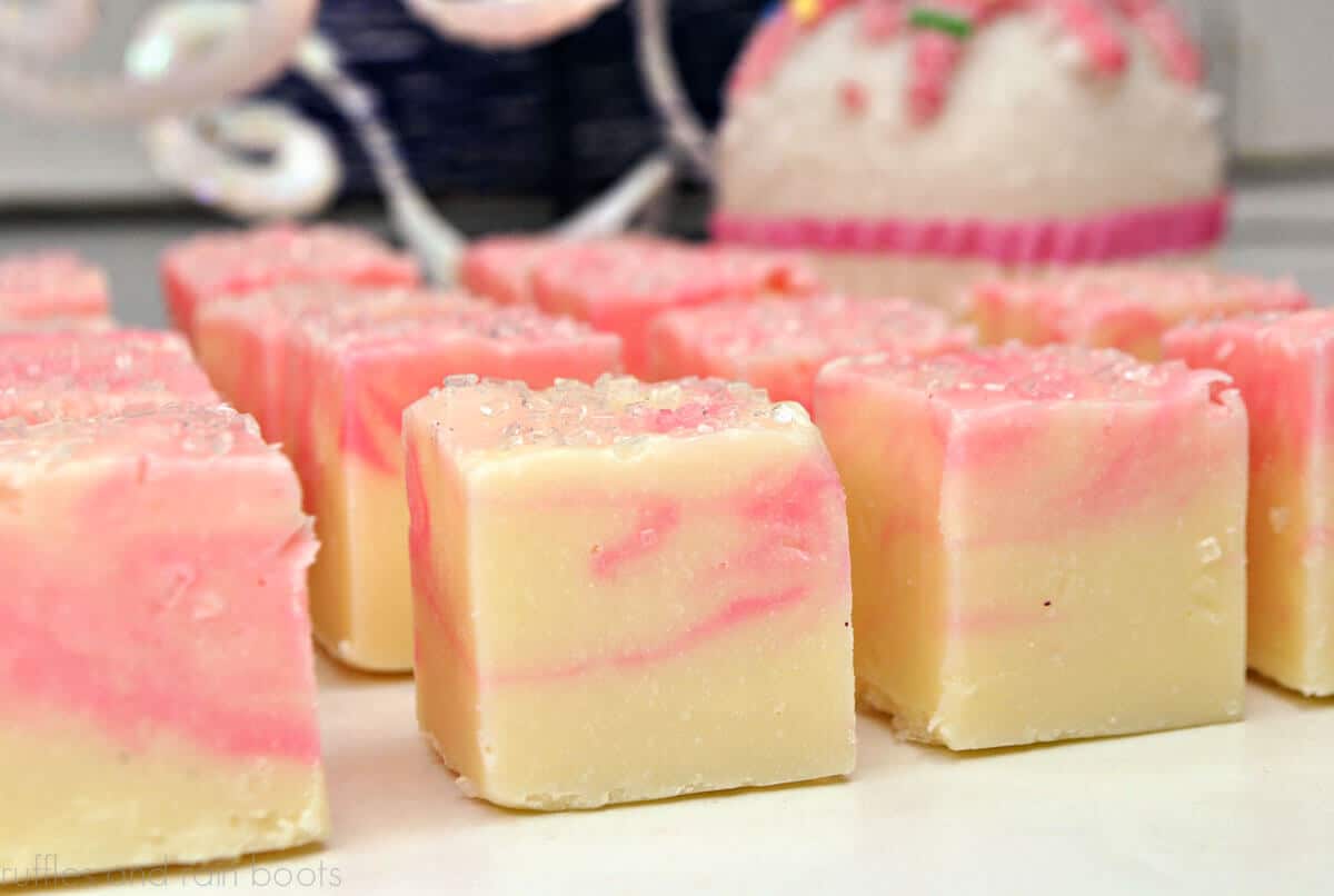 Close up of pink and white fudge squares on a white surface with pink and white decorations in the background.