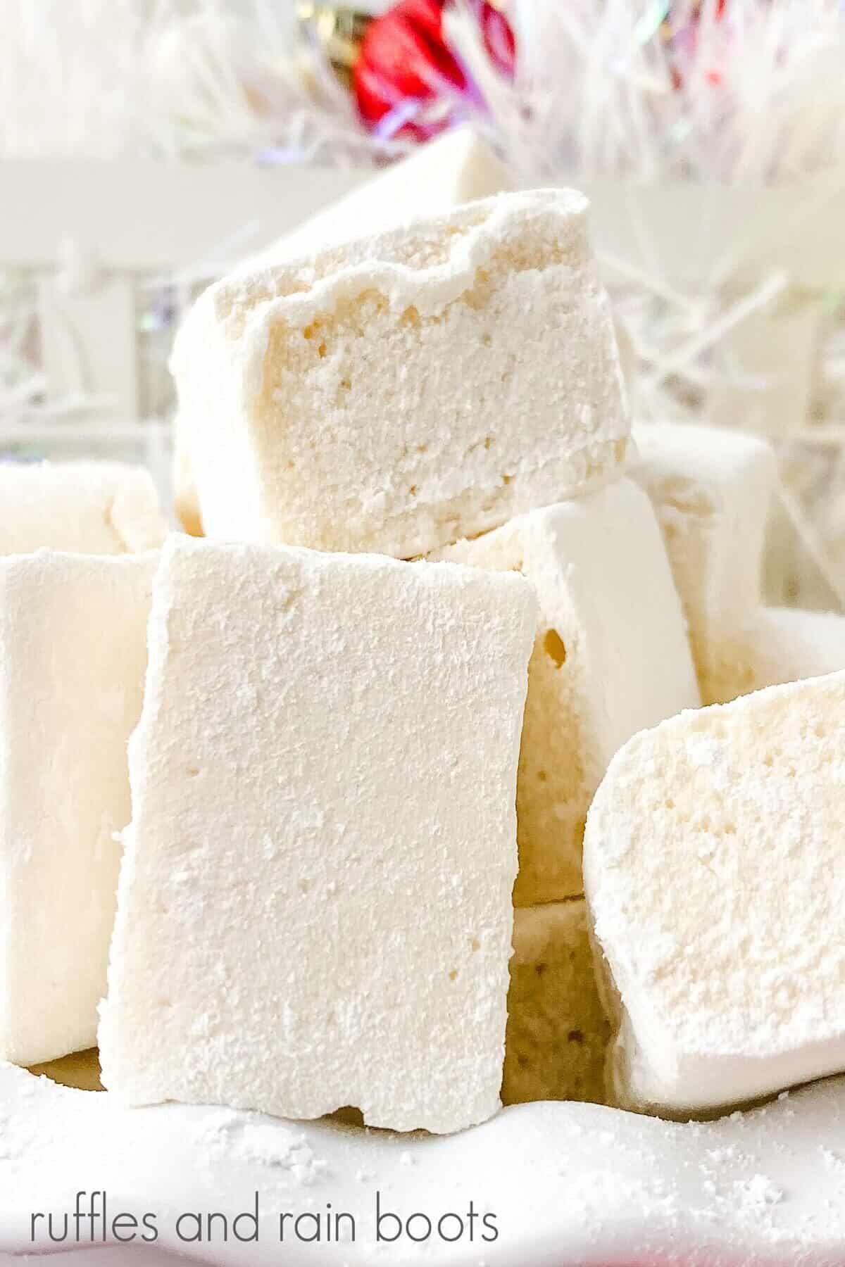 A close up of homemade eggnog marshmallows in a white ruffled bowl with Christmas decor in the background.