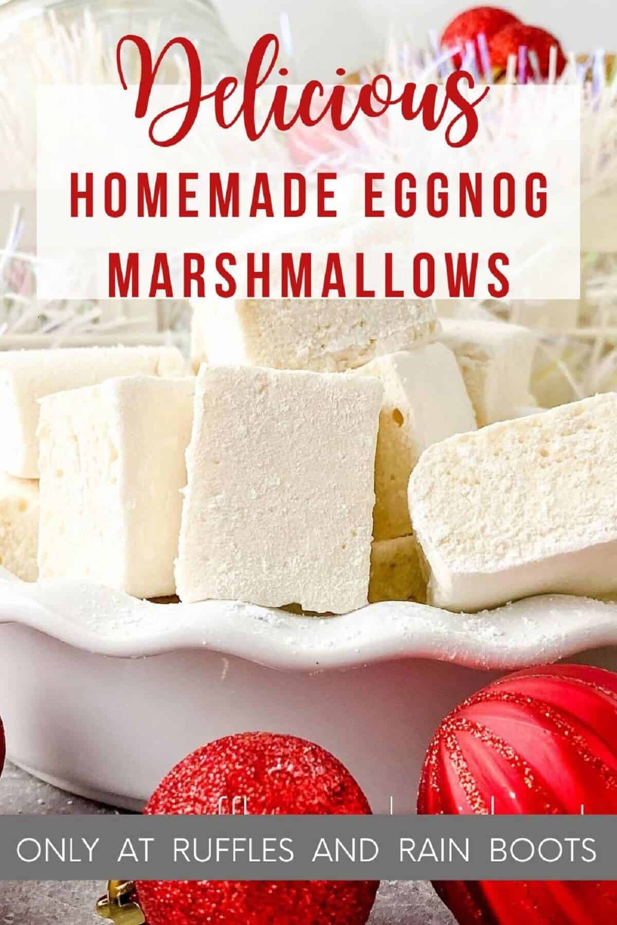 Ten homemade eggnog marshmallows in a white ruffled bowl with Christmas decor in a white basket in the background and red Christmas ornaments in the foreground on a grey marble surface.