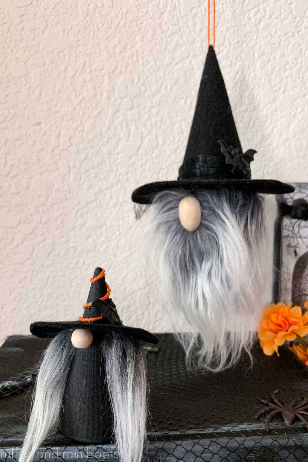 Vertical image of a wooden witch gnome and a hanging witch gnome ornament on a Halloween background.