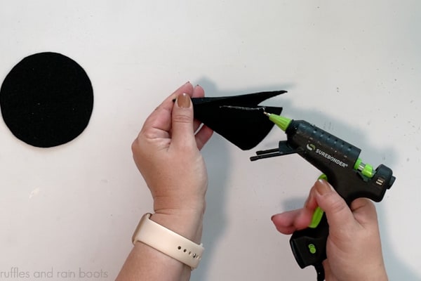 Crafter gluing a square of stiff felt together to create the cone for a gnome witch hat DIY.