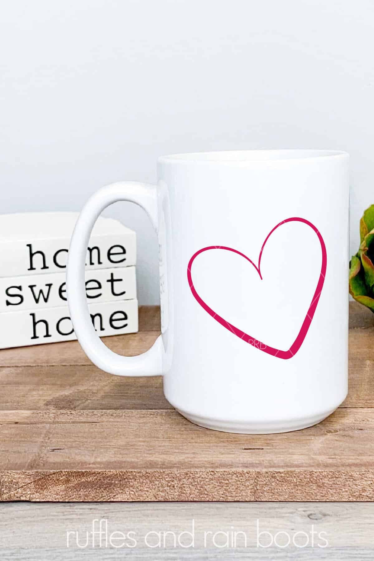 Vertical image of white mug with pink vinyl doodle heart cut file on farmhouse background.