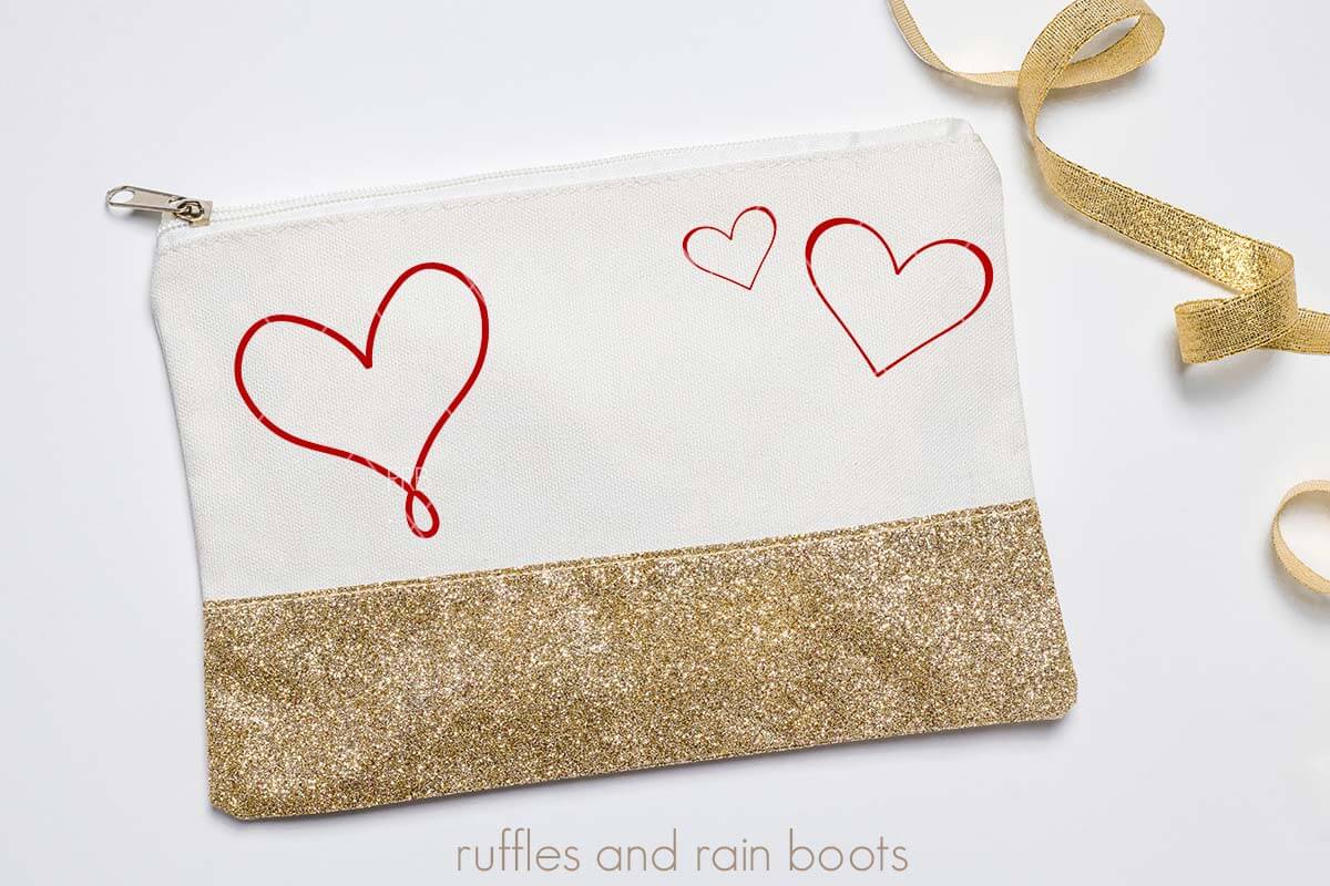 Horizontal image of gold glitter makeup bag with pink vinyl hearts on white background.
