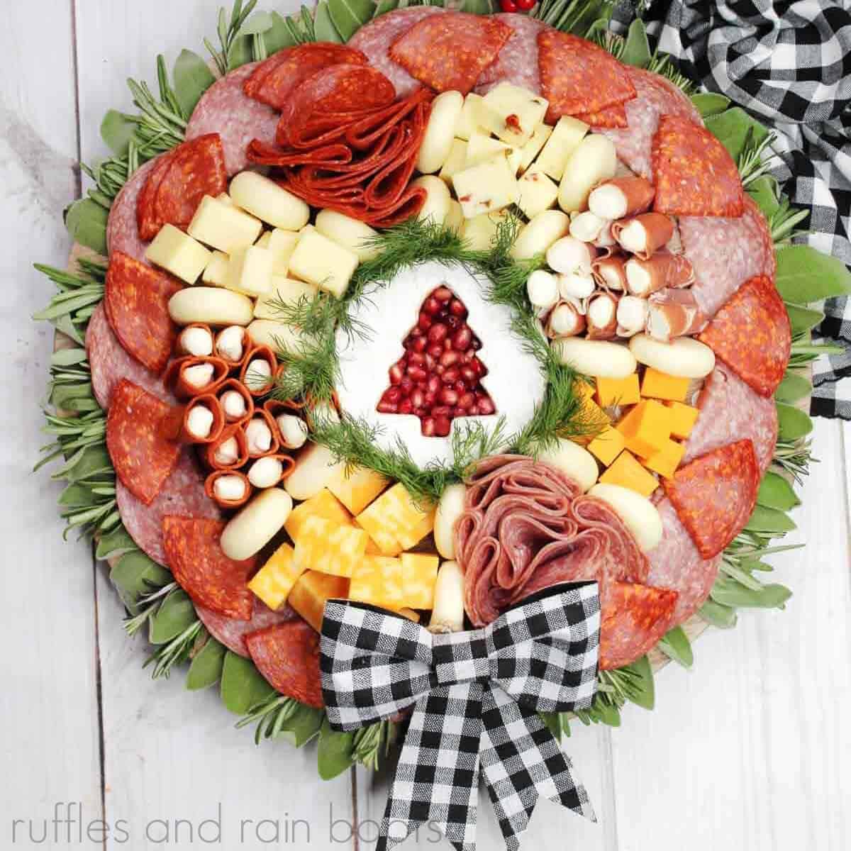 S overhead close up view of a holiday charcuterie board with a variety of meats and cheese with a black and white buffalo plaid bow on a white wood surface.