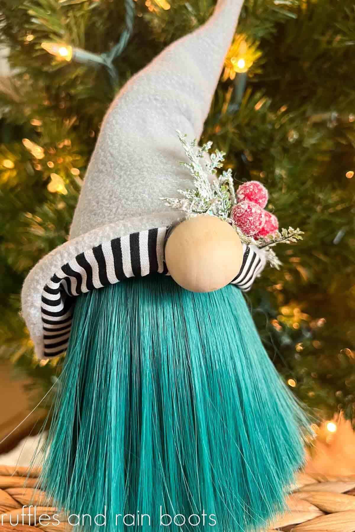 Vertical image of a Christmas gnome with a two sided hat and a gnome beard made of doll hair placed in front of a lit up holiday tree.
