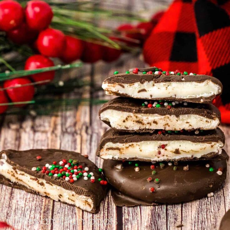 Square close up of a stck of homemade peppermint patties with a whole patty on the bottom and 4 half patties on top and beside, with holiday greenery and a black and red plaid fabric on a weathered wood surface.