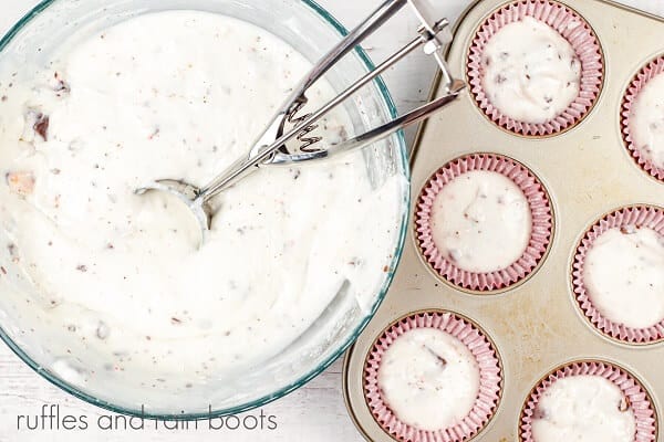 H an overhead image of a bowl of white chocolate peppermint batter and an ice cream scoop next to a cupcake pan