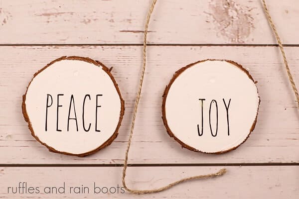 White wooden wood slice ornaments, one with a black lettering saying joy and one saying peace on a wooden surface.