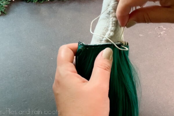 Crafter using embroidery thread and whipstitch to attach a gnome beard made of doll hair.