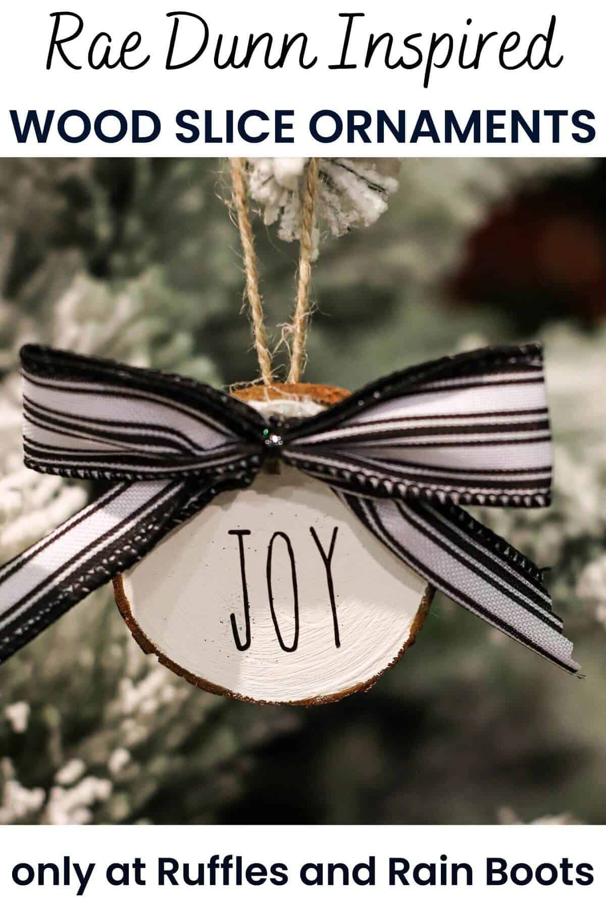 White wooden wood slice ornament with a black and white bow, Rae Dunn lettering and twine hanger on a Christmas tree.