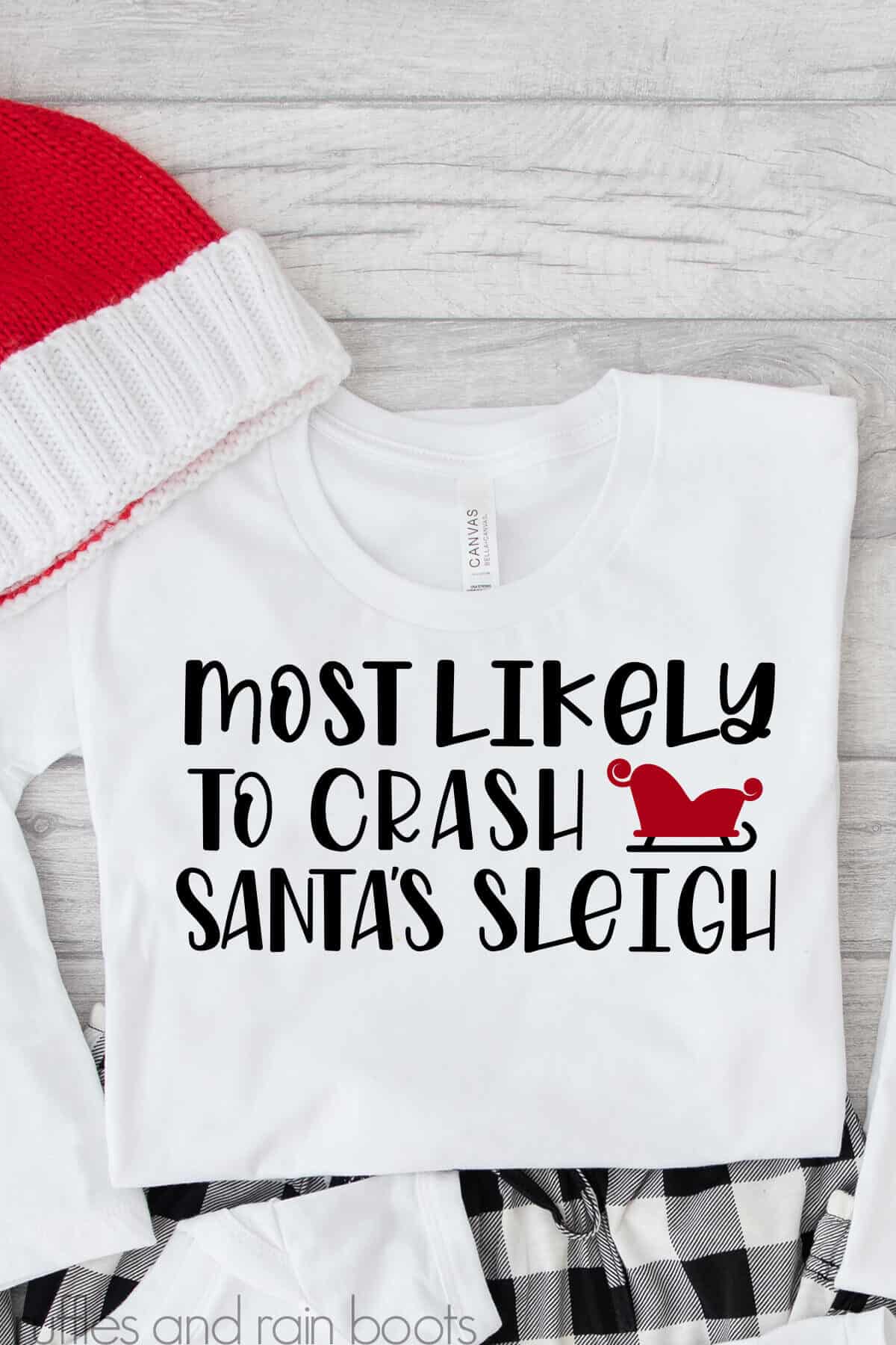 Vertical image of white t shirt with most likely to crash Santa's sleigh SVG in black and red vinyl.