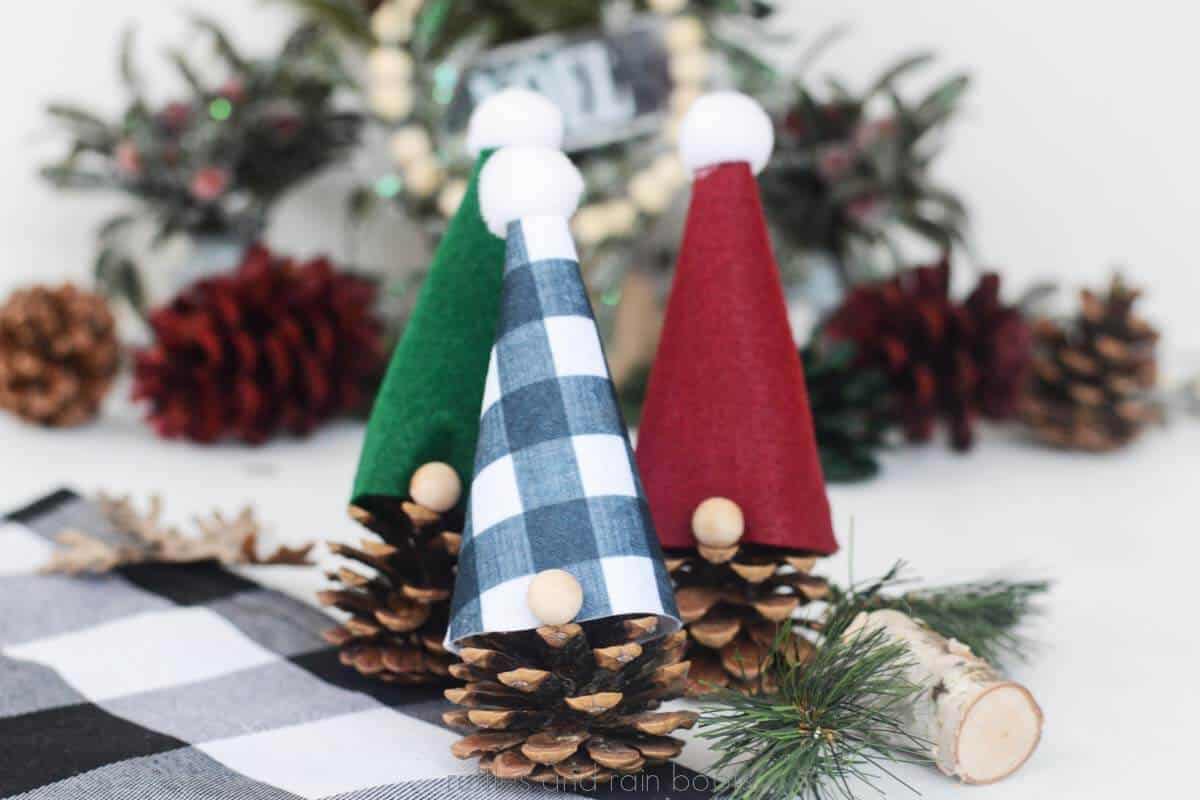 Horizontal image of a set of three Christmas gnomes made from pinecones placed on a holiday background.