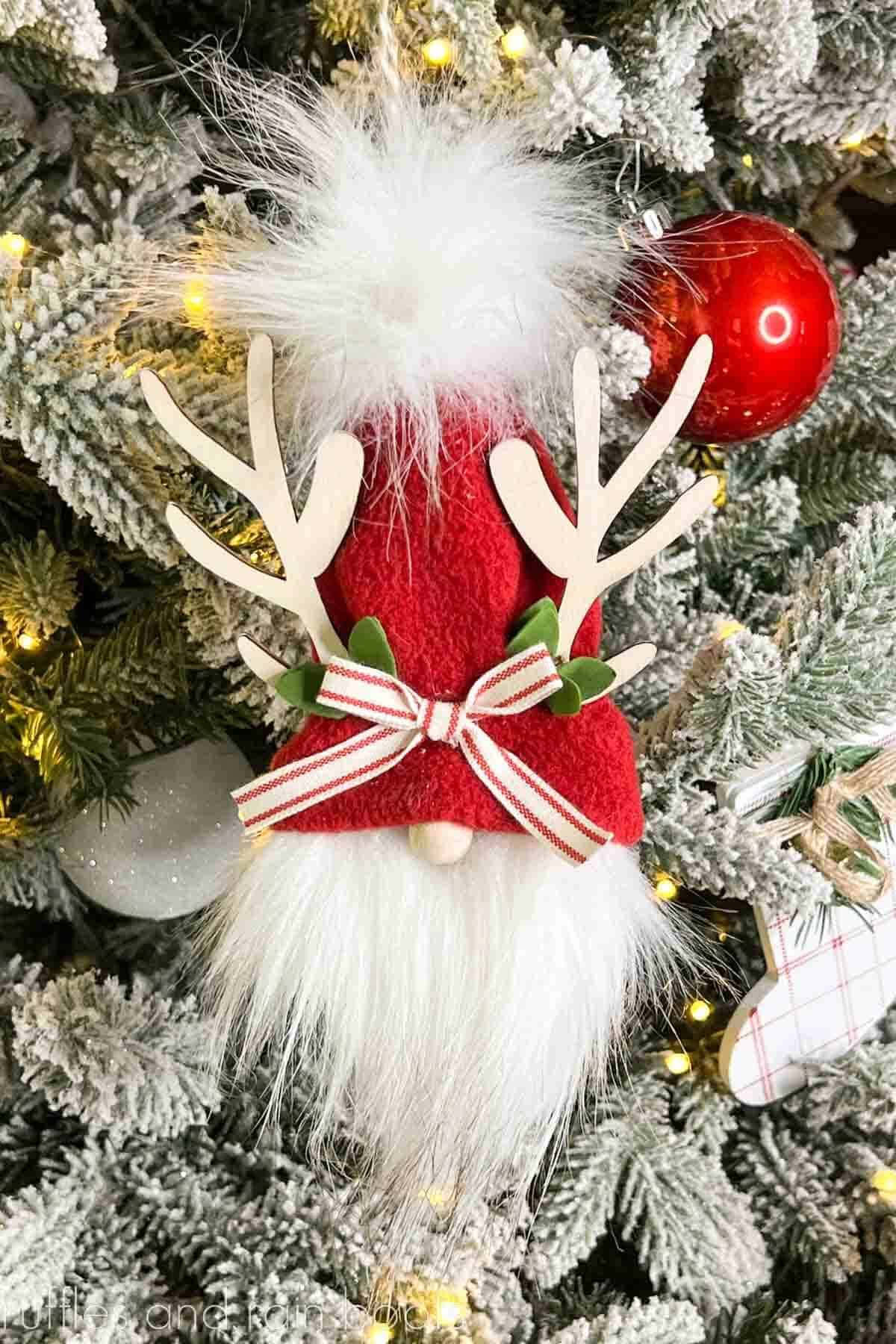 Vertical image of a red hat reindeer gnome hanging on a flocked Christmas tree.