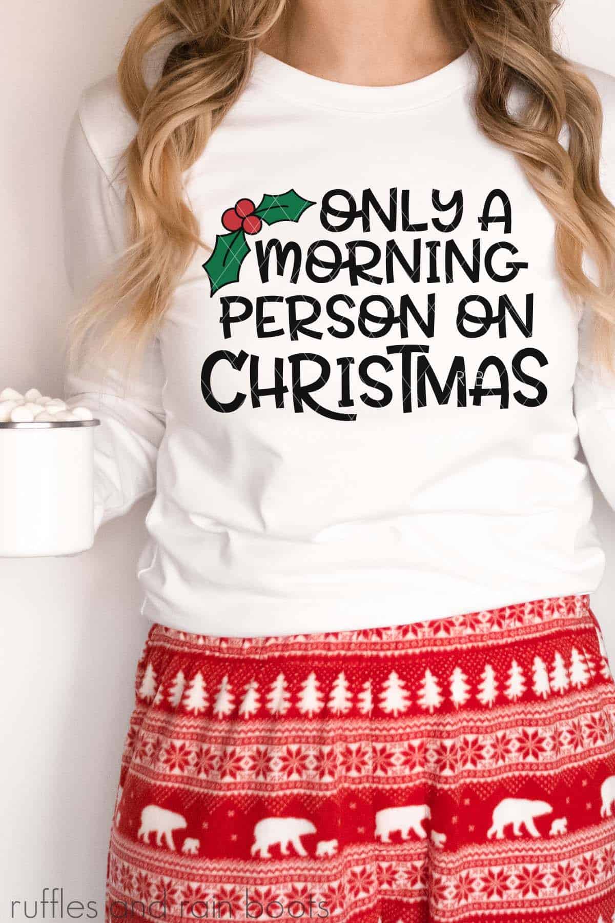 Vertical image of woman in holiday pajamas holding cocoa wearing red pants and white shirt which reads only a morning person on Christmas.