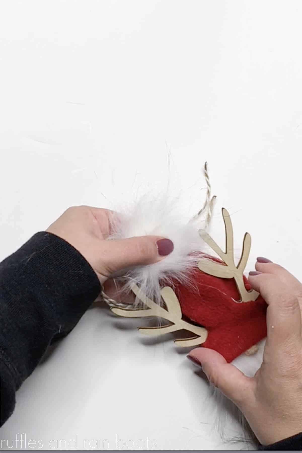 Crafter gluing on a fur pompom to the top of a red gnome hat made of fleece.