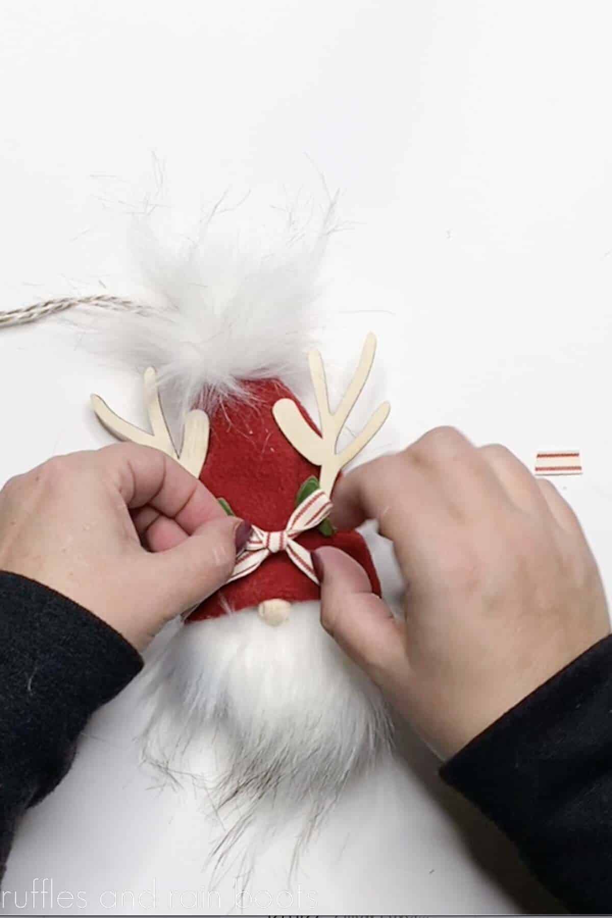 Crafter gluing on greenery and a bow to a finished gnome ornament with reindeer antlers.