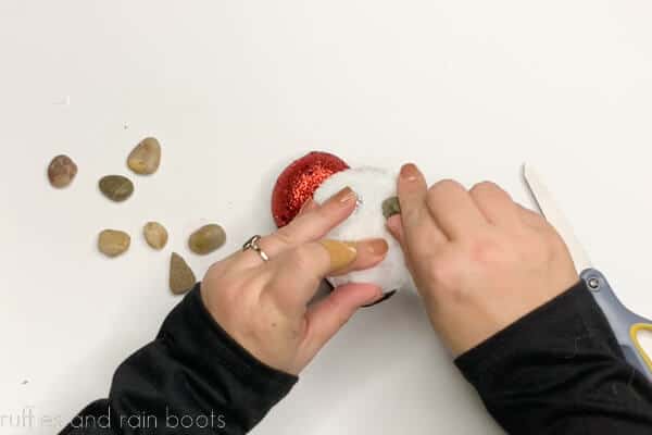Crafter adding small rocks into holiday boot ornaments on white background.