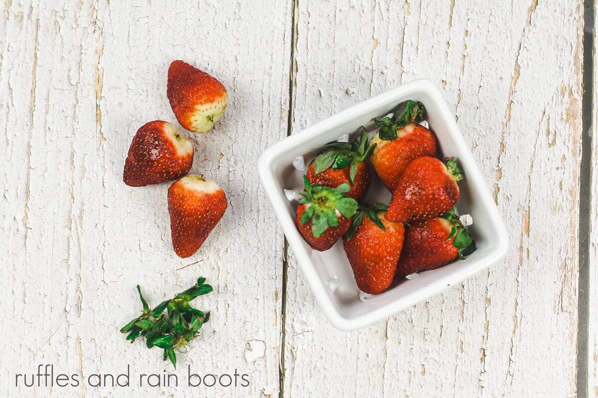 H overhead image a white berry basket filled with strawberries on a wood surface.