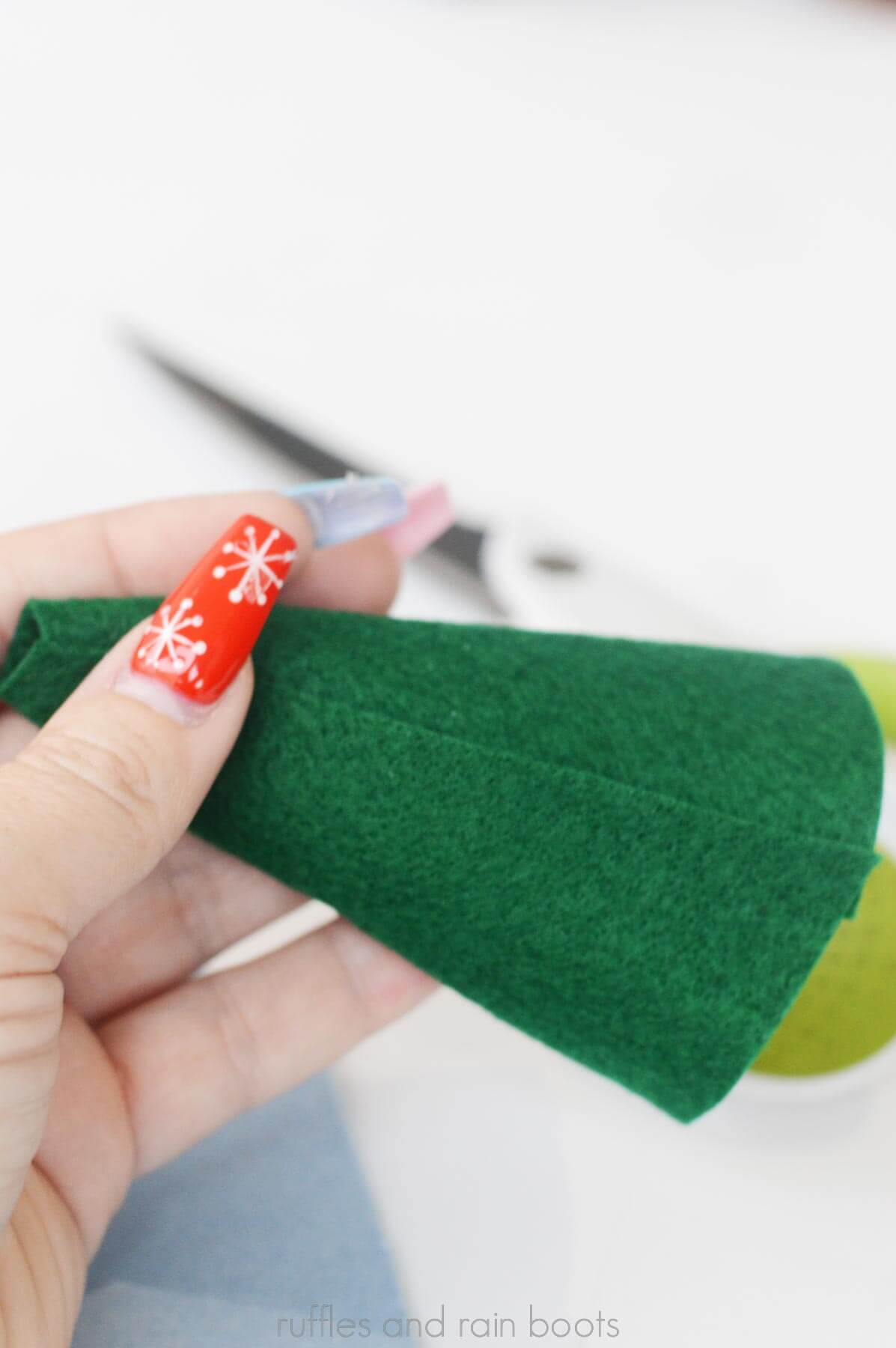 Hand showing a green felt gnome hat being glued together with hot glue.