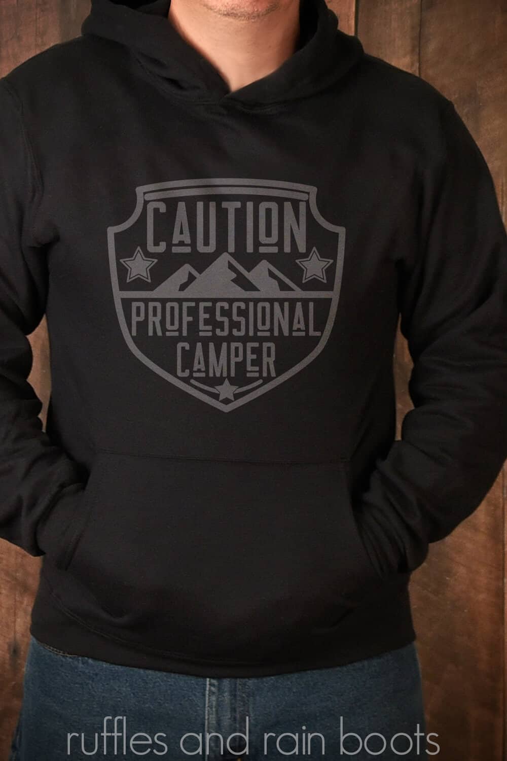 Vertical image of a man in a black hoodie sweatshirt with caution professional camper SVG in dark gray vinyl.