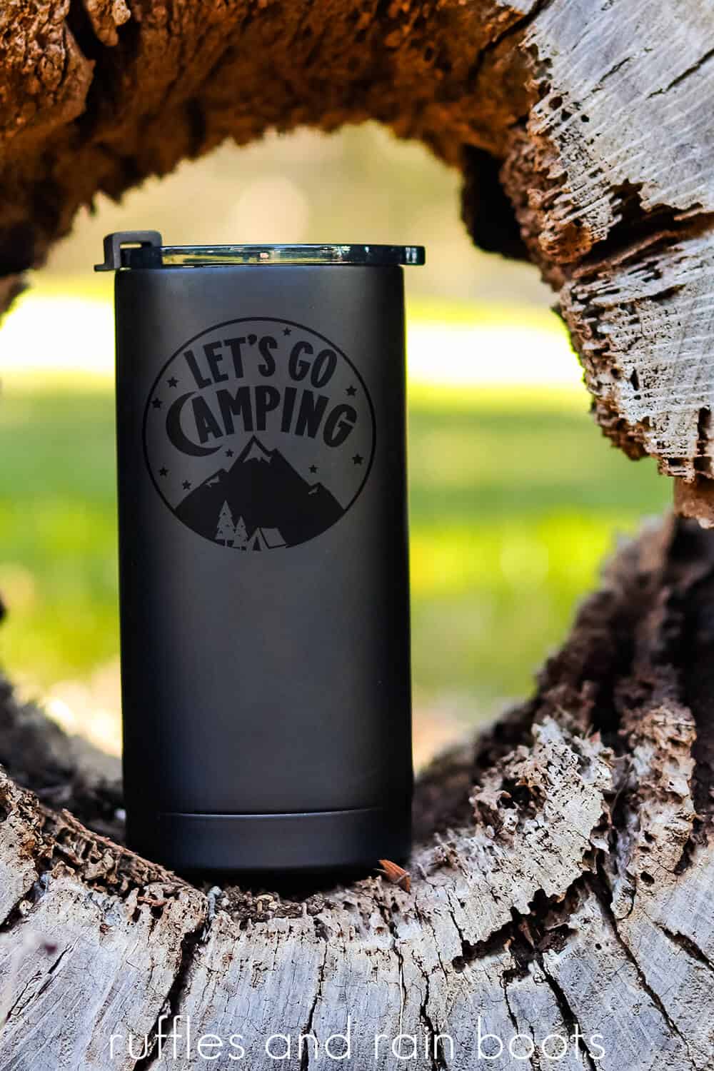 Vertical image of a stump with a black tumbler with black vinyl lets go camping svg with mountains.