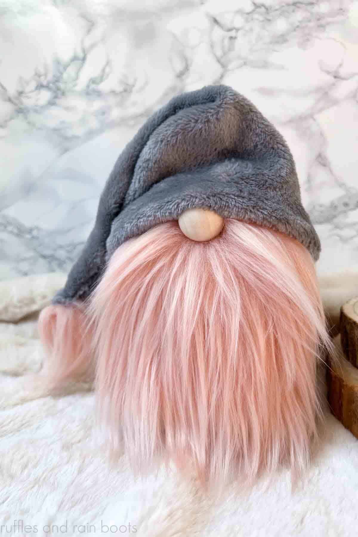 Vertical image of gray hat and pink beard Valentine gnome made on fur in front of marble background.