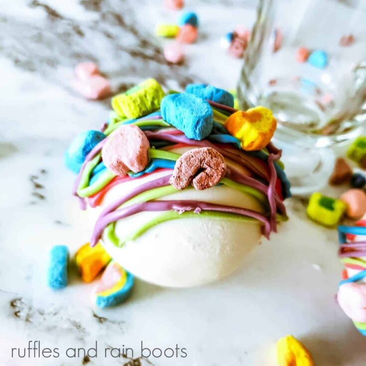 Close up of a Lucky Charms Hot Cocoa Bombs on a white marble surface with scattered marshmallows.