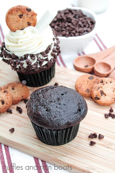 Overhead photo of Double Image of unfrosted chocolate cupcake on a cutting board, next to a frosted cupcake surrounded by mini chocolate chips and mini chocolate chip cookies on a white nakpkin with red stripes.