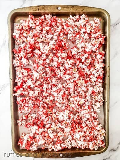 Baking sheet with popcorn covered in melted red chocolate on a marble surface.