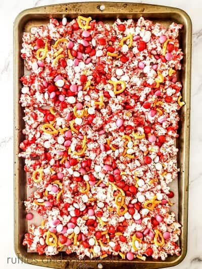 Popcorn coated with melted red chocolate, pretzels, M&Ms and sprinkles on a baking sheet on a marble surfce.marble surface.