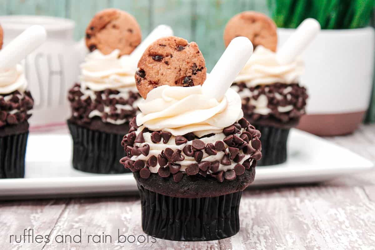 Cookies and cream cupcake in front of a plate of 3 cupcakes on a weathered wooden surface with a plant in the background.