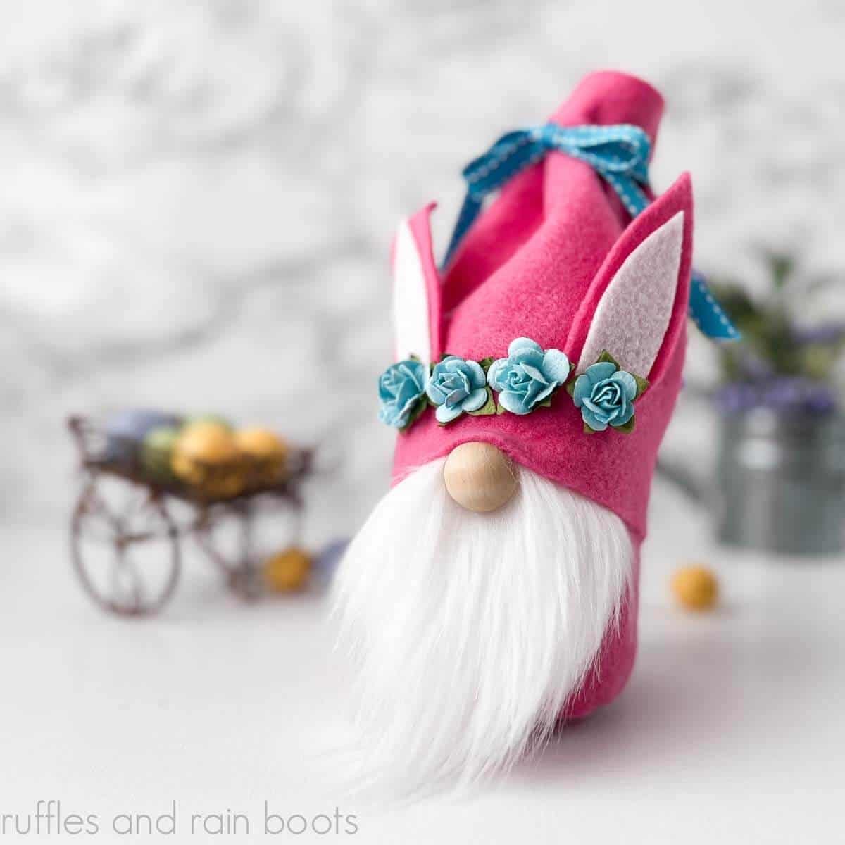 Square close up image of a gnome treat container made with pink felt, blue ribbon, blue flowers, and a white beard.