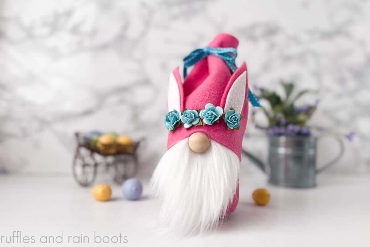 Horizontal image of a gnome treat jar made with felt, fur, and faux flowers on Spring background.