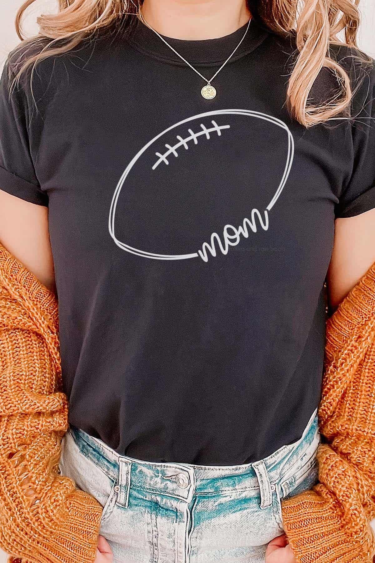 Vertical image of woman in orange sweater and black t-shirt with light gray football mom svg cut from HTV.