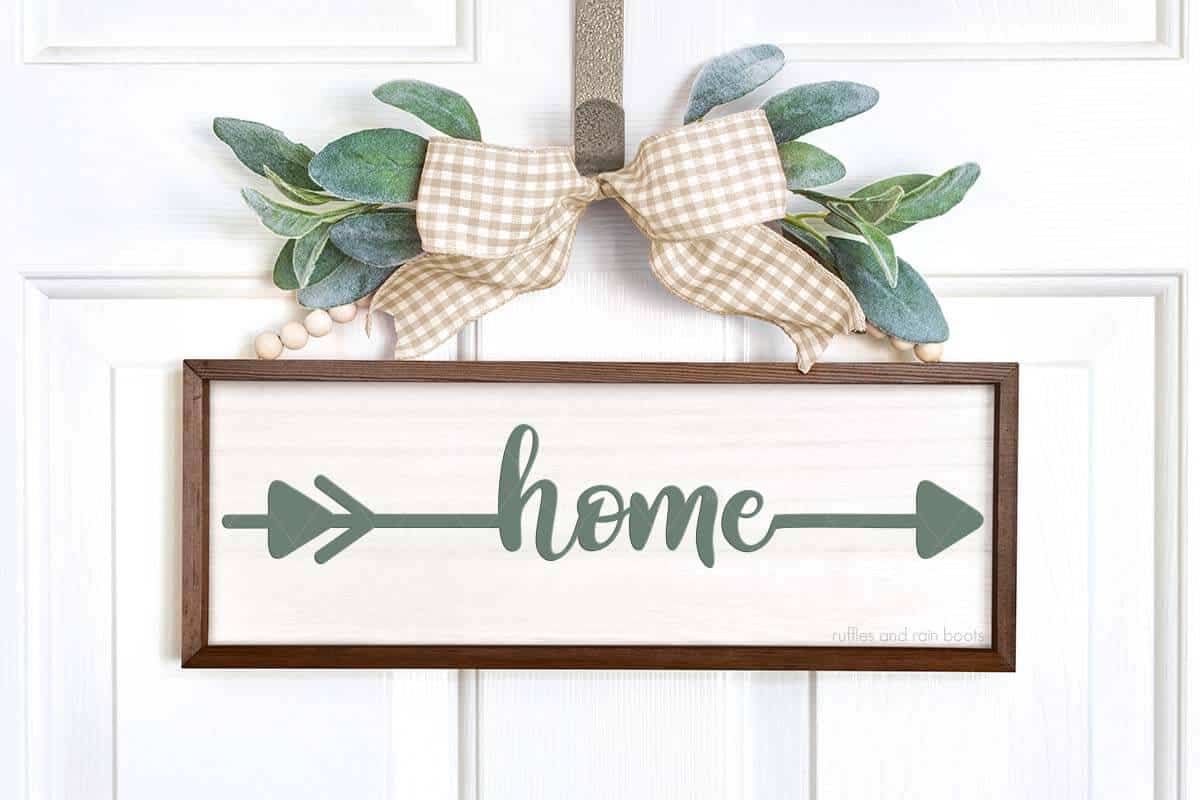 Horizontal image of home sign made with paint, ribbon, and greenery hanging on white door.
