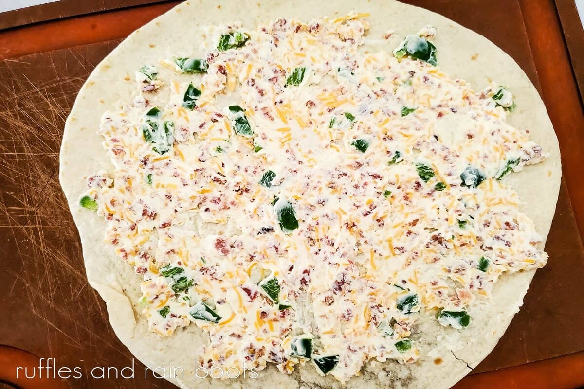 Jalapeno Popper Pinwheel Sandwich mix spread onto a large flour tortilla on a brown baking mat.
