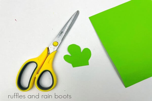 A piece of green paper with leaves cut out next to a pair of scissors on a white surface.